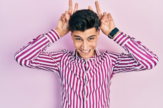 Young hispanic man wearing casual clothes posing funny and crazy with fingers on head as bunny ears, smiling cheerful