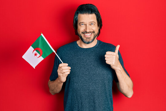 Middle age caucasian man wearing hijab holding algeria flag smiling happy and positive, thumb up doing excellent and approval sign