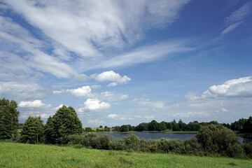 Rural landscape. Fields, forests and a lake. White clouds. Blue sky. Windy day in August