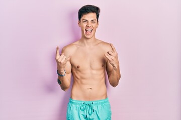 Fototapeta premium Young hispanic man wearing swimwear shirtless shouting with crazy expression doing rock symbol with hands up. music star. heavy concept.