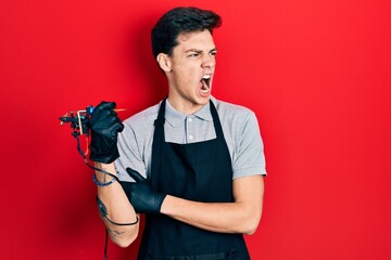 Young hispanic man tattoo artist wearing professional uniform and gloves holding tattooer machine...