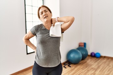 Fototapeta na wymiar Middle age woman wearing sporty look training at the gym room suffering of neck ache injury, touching neck with hand, muscular pain