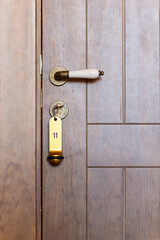 Close-up of a wooden hotel door with a golden, vintage handle and the key in the key hole.