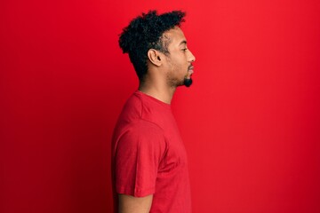 Fototapeta na wymiar Young african american man with beard wearing casual red t shirt looking to side, relax profile pose with natural face with confident smile.