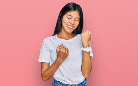 Beautiful young asian woman wearing casual white t shirt celebrating surprised and amazed for success with arms raised and eyes closed. winner concept.