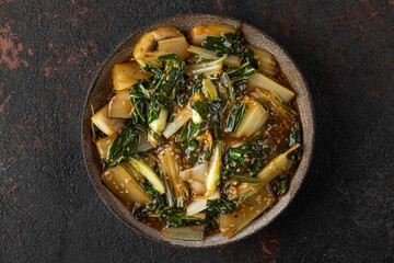 Cooked bok choy or chinese cabbage with sesame seeds and soy sauce on dark background. Asian chinese food. top view