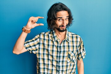 Young hispanic man wearing casual clothes smiling and confident gesturing with hand doing small size sign with fingers looking and the camera. measure concept.