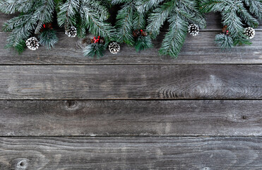 Snow covered evergreen branches plus pine cones and red berries on faded wooden planks for a merry Christmas or happy New Year holiday celebration concept