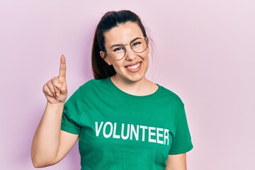 Young hispanic woman wearing volunteer t shirt pointing finger up with successful idea. exited and happy. number one.