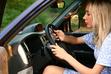 Fototapeta na wymiar Young woman talking on a cell phone while sitting in the car in the driver's seat. Attractive blonde female student