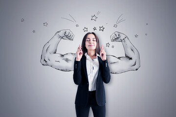 Pretty young european businesswoman with crossed fingers standing on concrete wall background with...