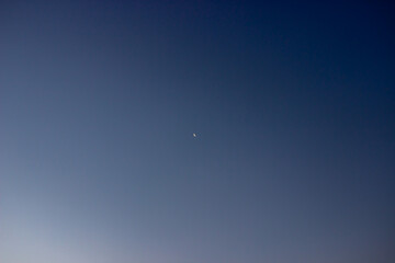 Small view of moon in the sky at dawn. Beautiful view of sky with white, blue and dark blue colors just before the sunrise. Selective focus.