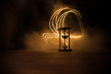 Time concept. Silhouette of Hourglass clock and old vintage wood clock with arrow and smoke on dark background with hot yellow orange red blue cold back lighting, or symbols of time with copy space