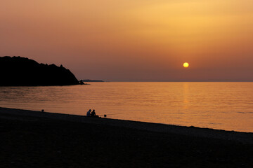 Silhouette of two men fishing on the beach during the sunrise. Sun rises over the Mediterranean Sea on a lovely summer morning. Selective focus.