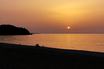 Silhouette of two men fishing on the beach during the sunrise. Sun rises over the Mediterranean Sea on a lovely summer morning. Selective focus.