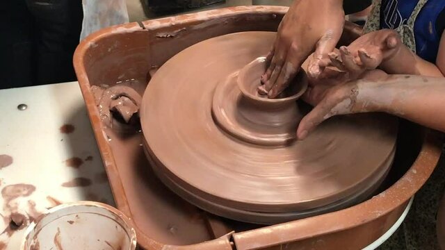 Hands of mother and child shaping clay on a ceramics pottery wheel