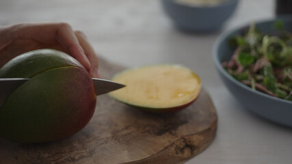 Man cut mango for salad with micro greens and mozzarella in blue bowl