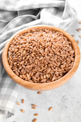 Wholegrain uncooked raw spelt farro in wooden bowl on grey stone table background, food cereal background, close up