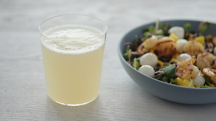 Lemonade in tumbler glass next to salad with shrimps, mango, mozzarella and micro greens