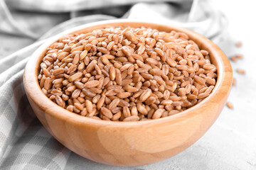 Wholegrain uncooked raw spelt farro in wooden bowl on grey stone table background, food cereal background, close up