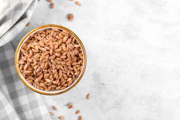 Wholegrain uncooked raw spelt farro in ceramic bowl with napkin on grey stone table background, food cereal background, view from above, copy space