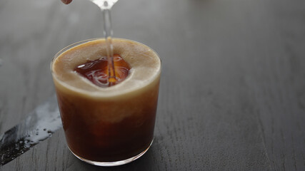 Making espresso tonic in tumbler glass, pour espresso over ice cube