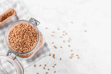 Wholegrain uncooked raw spelt farro in glass jar on grey stone table background, food cereal background, close up, kitchen zero waste, copy space