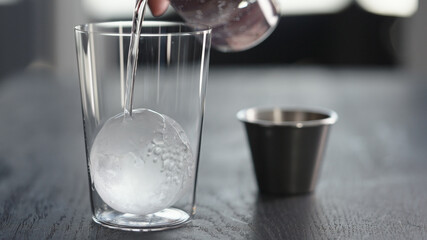 Making espresso tonic in tumbler glass, pour tonic over ice ball