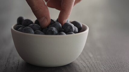 Man hand pick ripe blueberries from white bowl on oak table