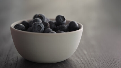 Ripe blueberries from white bowl on oak table