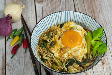 A serving of instant noodle with chicken, sunny side up and veggies. Selective focus points. Blurred background