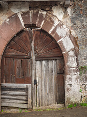 Fototapeta na wymiar Puerta vieja con arco de piedra y madera desgastada en el pueblo de Treceño, Cantabria en el verano de 2020