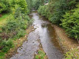 Fototapeta na wymiar Vistas del río rodeado de árboles verdes y piedras en el área recreativa Las Cuevas en Cantabria, España, verano de 2021.