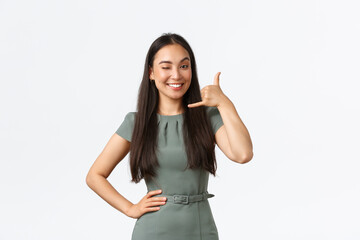 Small business owners, startup and work from home concept. Smiling cheeky asian woman winking and smiling, encourage clients give her call, shop assistant answering client questiones via phone - obrazy, fototapety, plakaty