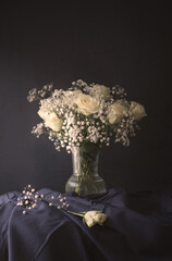 Vintage painting style photograph of cream white roses and Gypsophila (baby's breath) set against a dark navy blue background on a table. Still life old painting style image.