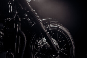 Fototapeta na wymiar Motorcycle with water drops at night. Front wheel with disc brakes. Classic black motorbike. Caferacers style. Maintenance of motor vehicles.