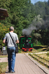 a man walks on a platform and steam locomotive on rails