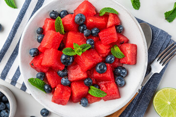 Fresh summer watermelon and blueberry salad with mint in a plate over napkin on white background. top view
