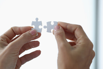 Female hands holding two white puzzle pieces closeup