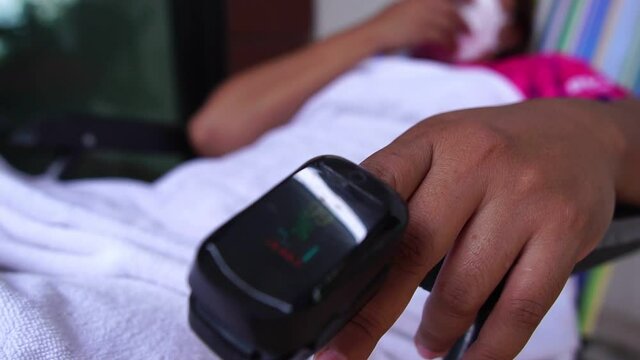 Asian thailand woman's finger attached with oximeter measuring oxygen saturation in blood and heartbeat rate at home COVID-19 health technology