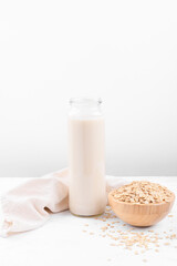 Vegan non dairy alternative milk. Oat milk in a bottle and a bowl with oat flake on white table background, copy space