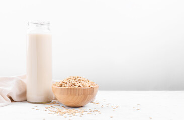 Vegan non dairy alternative milk. Oat milk in a bottle and a bowl with oat flake on grey stone table, copy space
