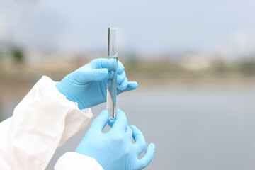 Scientist in rubber gloves holding test tube with sample of water from river closeup