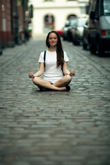 A teen girl is sitting in the lotus position in the middle of the city pavement.
