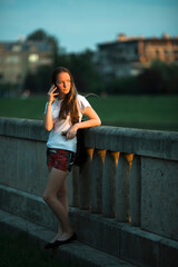 Cute teen girl is talking on the phone standing on the city embankment.