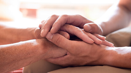 Worried caucasian man gently stroking hand of his sick old mother showing care or love. Son...