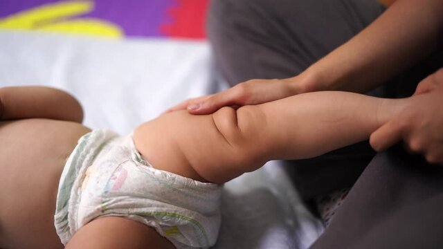 Female hands massage the leg of a lying infant