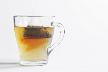 Tea bag - a pyramid of black tea is brewed in hot water in a transparent mug. White background....
