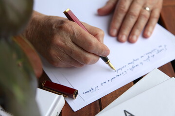 Male hand writing a letter with a fountain pen and blue ink, office atmosphere