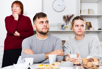 Young couple sitting at home table offended after quarrel with elderly mother